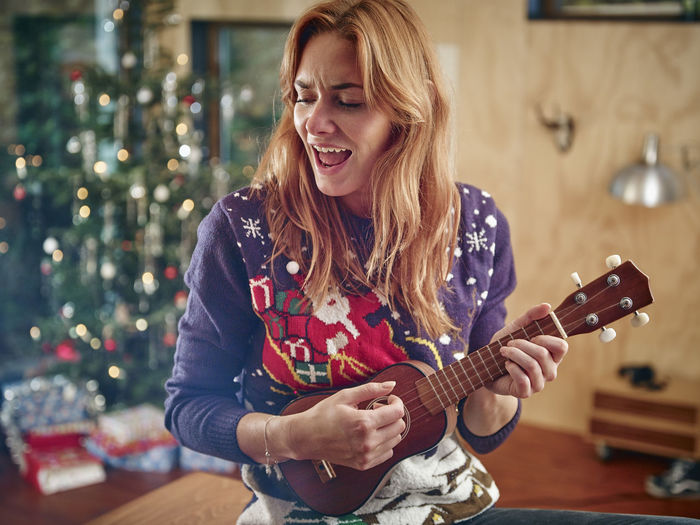 Blond woman playing ukulele in front of christmas tree