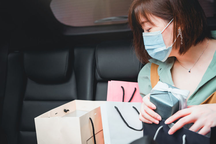 Woman wearing mask holding gift box sitting in car