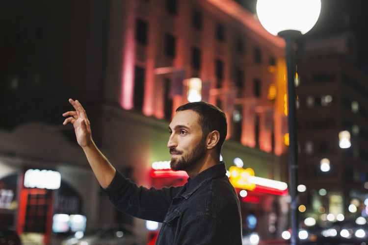 Portrait of young man looking at illuminated city