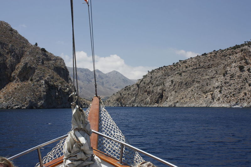 Cropped image of boat in sea by mountains against sky