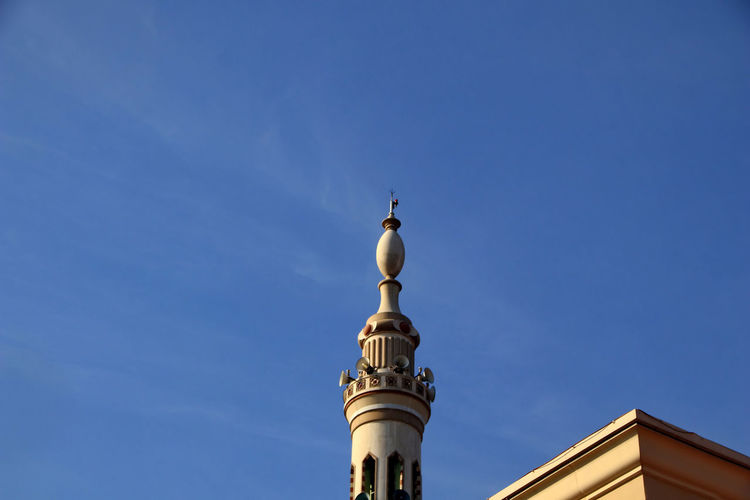 Low angle view of mosque tower against blue sky