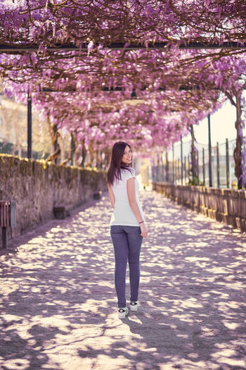 Full length portrait of beautiful woman standing on road under flowers