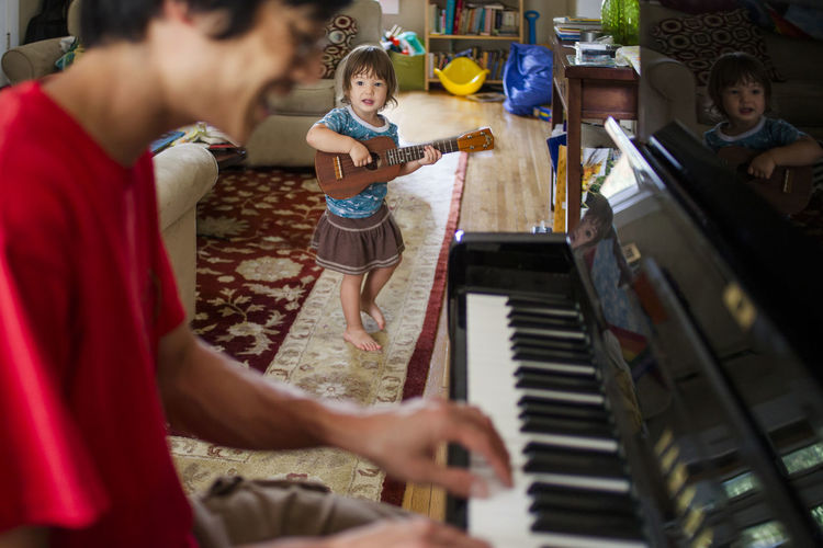 Father playing piano while daughter practicing guitar at home