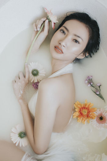 High angle portrait of beautiful woman with flowers relaxing in bathtub