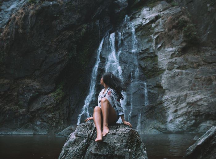 Woman sitting on rock against waterfall