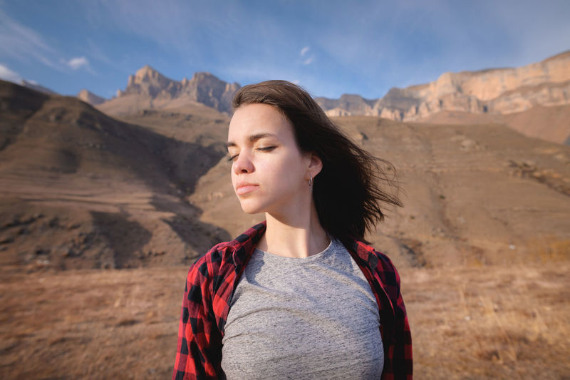 Young attractive woman stands in a shirt against a background of mountains