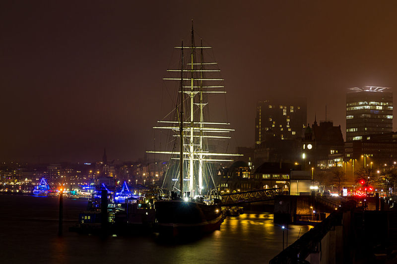 Illuminated sailing ship in sea at harbor against sky