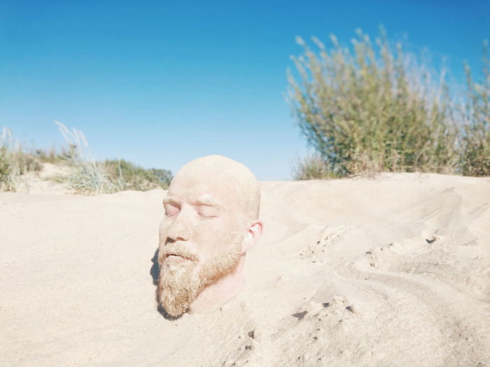 Close-up of man buried in sand at beach against clear sky