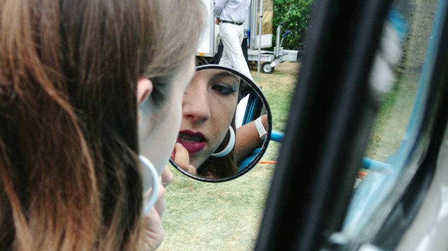 Close-up of model applying lipstick with reflection on mirror