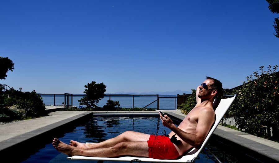 Man lying on back poolside against clear blue sky