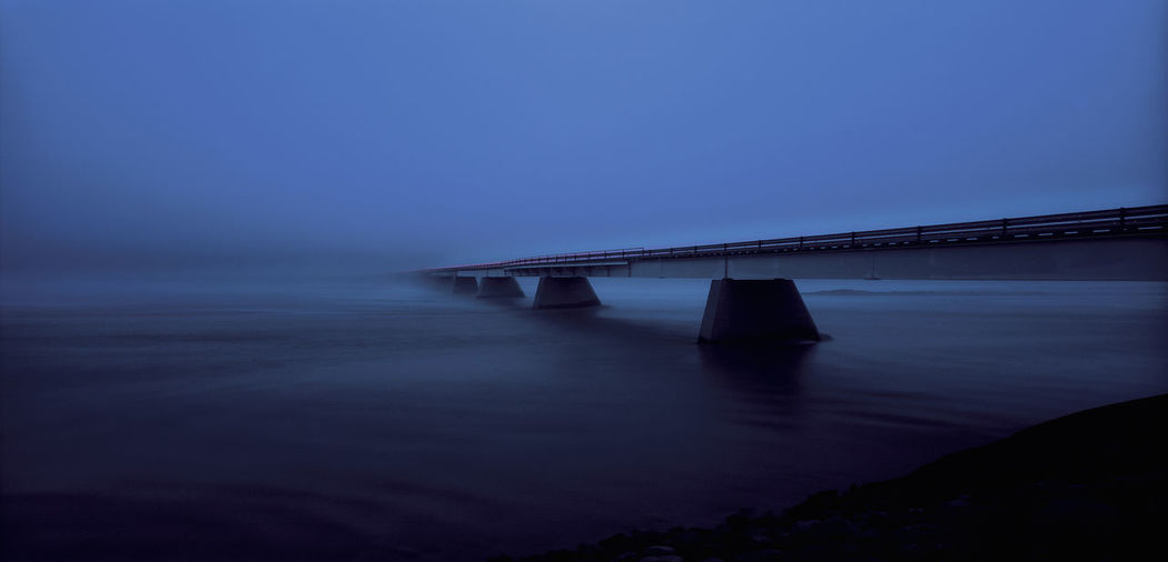 Bridge over sea against sky at dusk