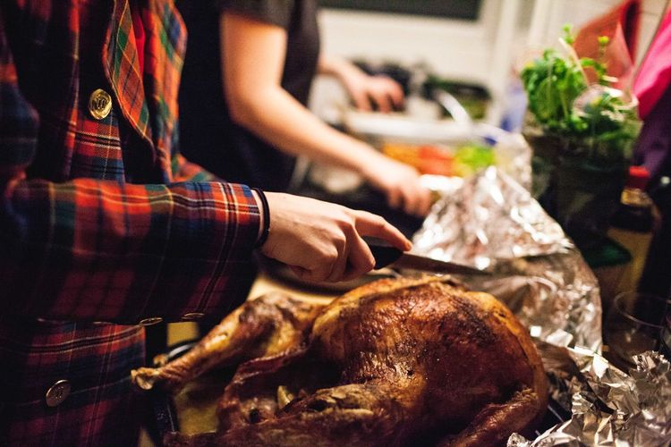 Midsection of person holding kitchen knife on thanksgiving turkey at home
