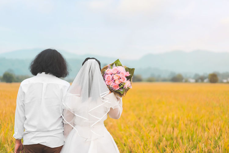 Rear view of married couple standing on field against sky