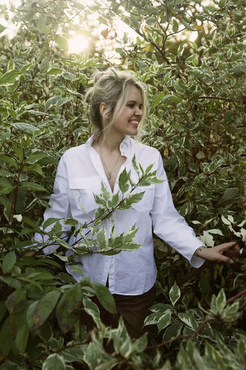 Young woman smiling while standing against plants