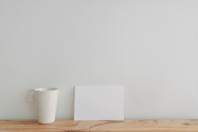 Close-up of coffee cup on white table against wall