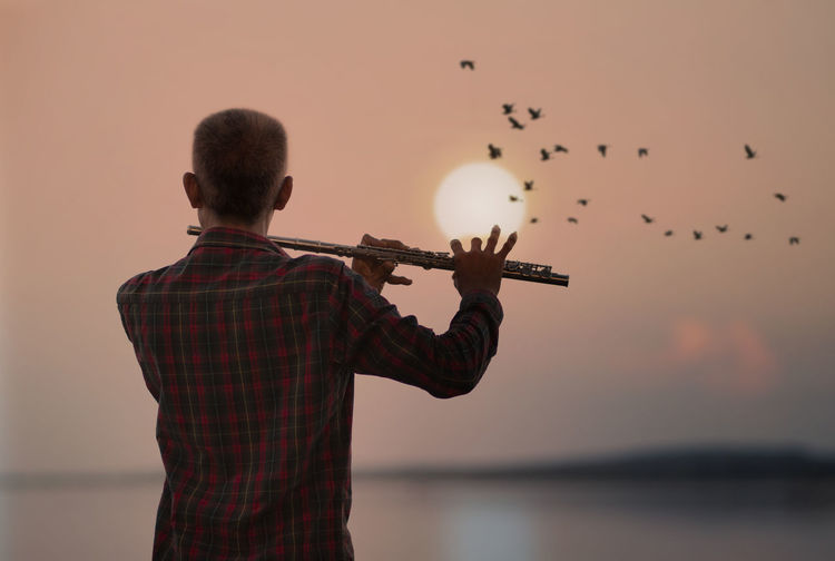 Man playing flute with sunset or sunrise background