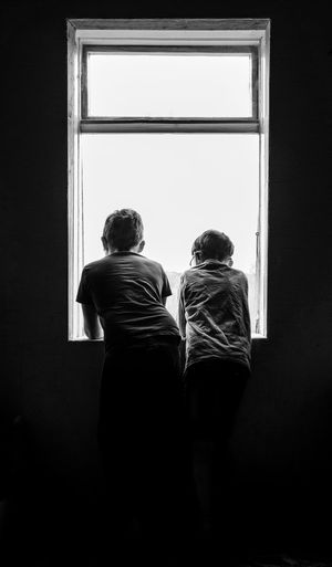Rear view of two kids looking through window