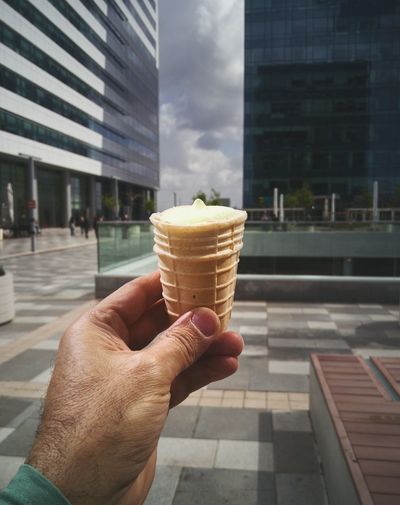 Close-up of hand holding ice cream cone against building