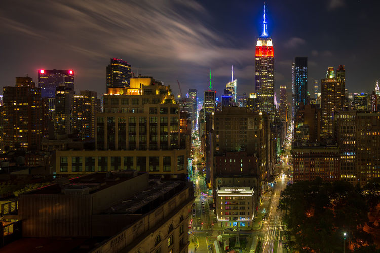 Illuminated empire state building amidst cityscape at night