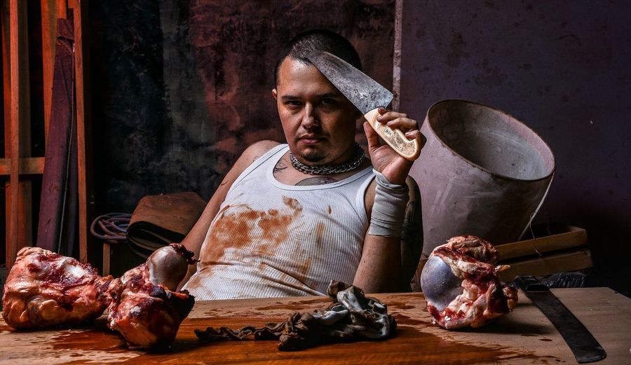 Portrait of confident butcher sitting in front of meat on table in shop