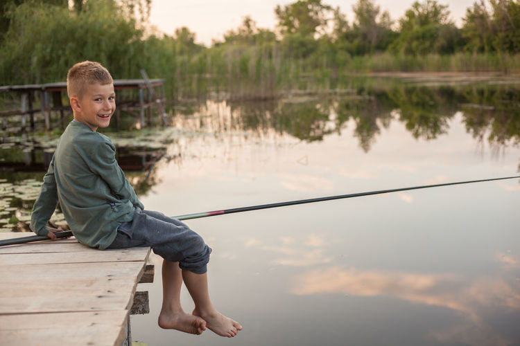 Portrait of happy boy on pier fishing in lake against sky