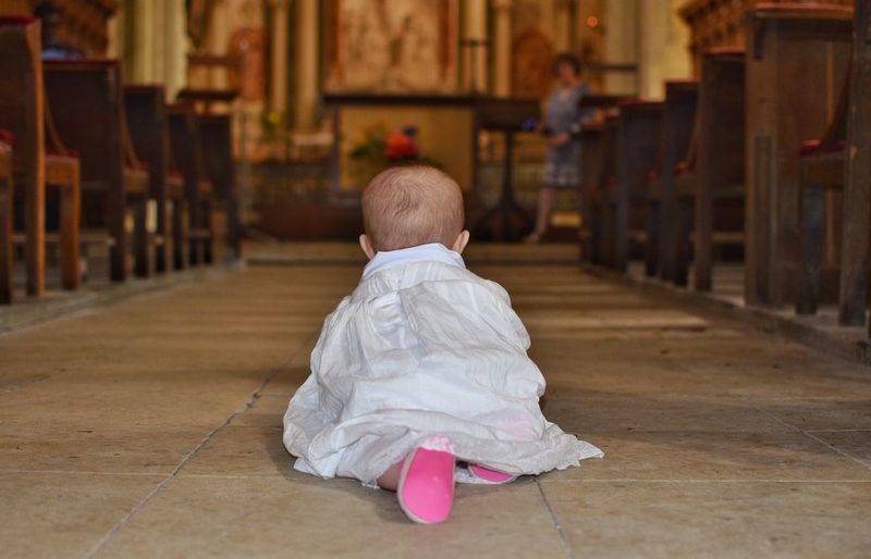 Baby girl with pink shoes crawling to baptism in church 