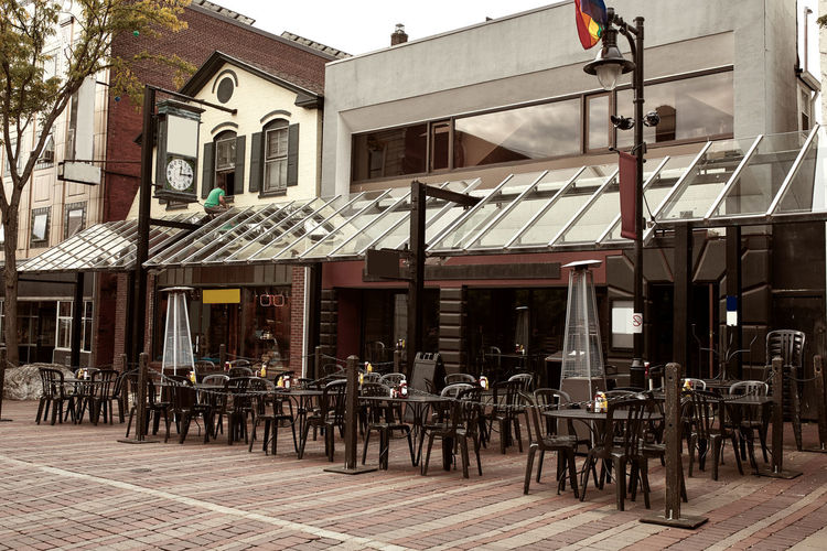 Chairs and tables at sidewalk cafe by buildings in city