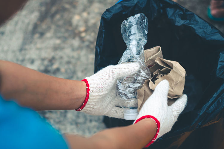 Cropped hands of person wearing gloves inserting garbage in plastic bag