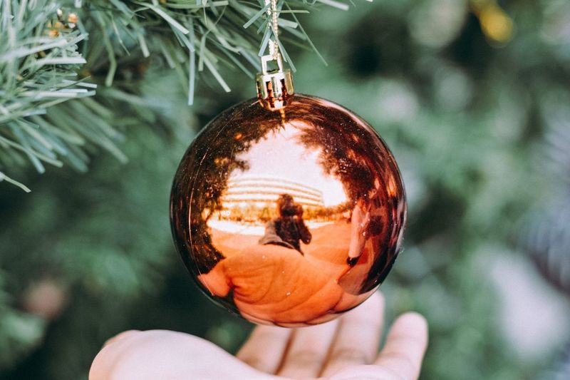 Cropped hand below bauble hanging from christmas tree