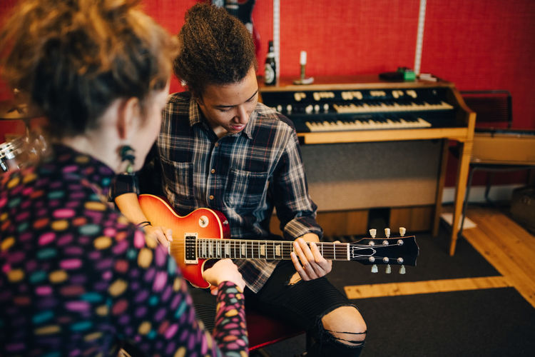 Woman sitting with friend playing guitars while practicing at recording studio