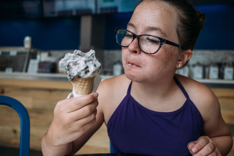 Front view of girl with glasses eating ice cream in ice cream parlor