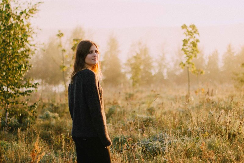Portrait of young woman standing on field during sunset