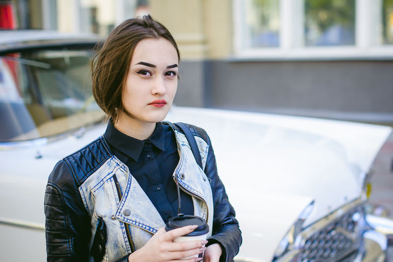 Portrait of confident young woman with disposable cup standing in city