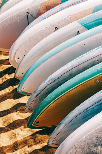 Close-up of colorful paddle boards for rent lying on the sand.