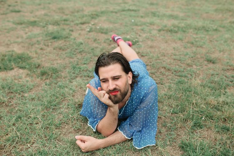 Full length of man wearing blue dress and red lipstick lying on field