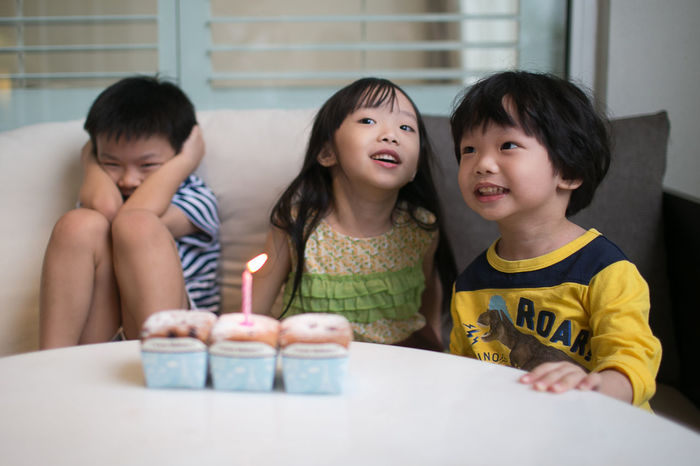 Children sitting by table with illuminated candle on cupcake
