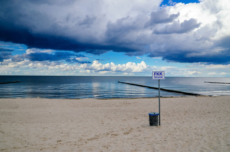 Sign board on sand at beach against cloudy sky
