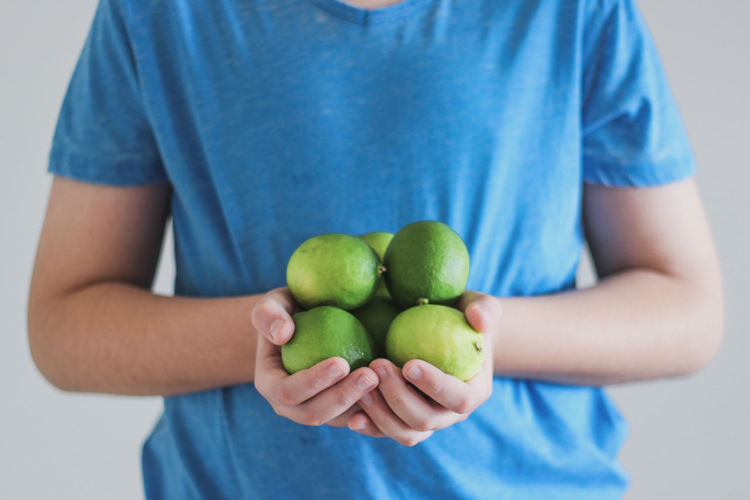 Midsection of man holding green limes against white background