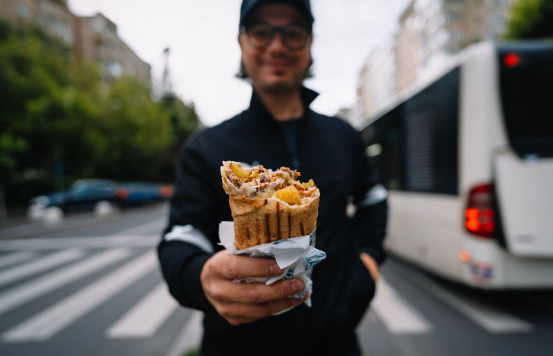 Man holding kebab wrap sandwich standing on zebra crossing on street