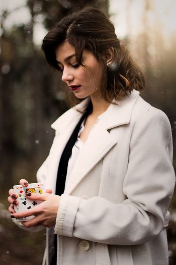 Young woman holding playing cards while standing in forest