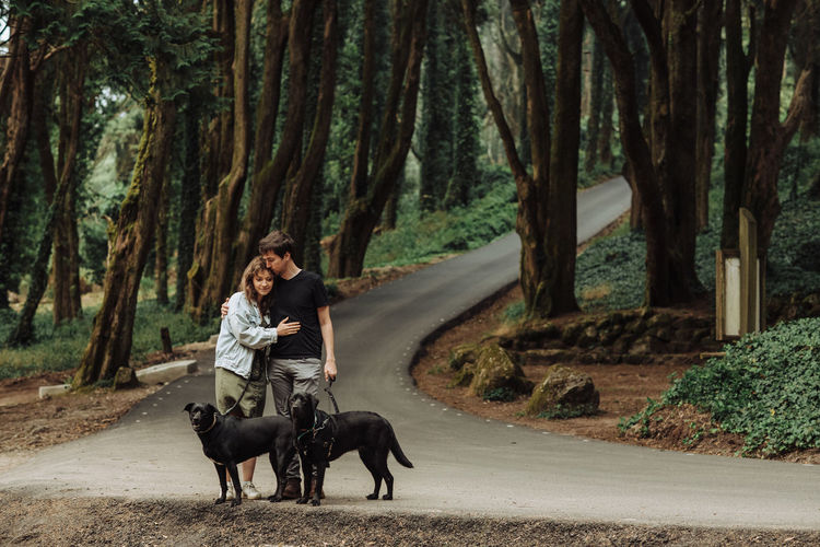 Couple embracing while standing with dogs on the forest road