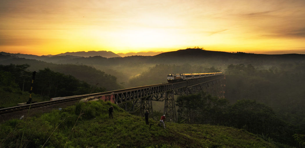 Train on bridge over landscape during sunset