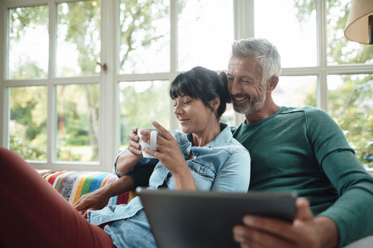 Happy man sharing tablet pc with woman holding coffee cup at home