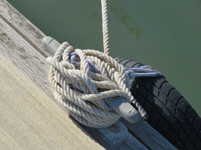 High angle view of rope tied on bollard at pier by river during sunny day