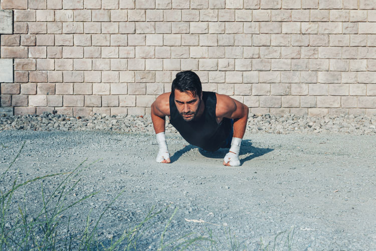 Young athletic man boxer on training doing push ups outdoors on a dusty road