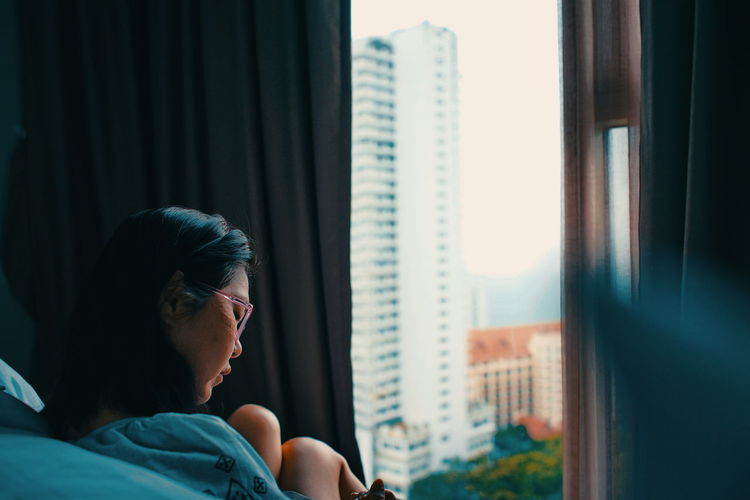 Portrait of young woman looking through window at home