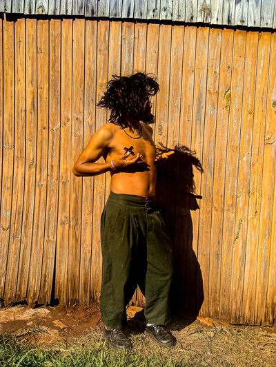 Full length of shirtless man standing against wooden wall