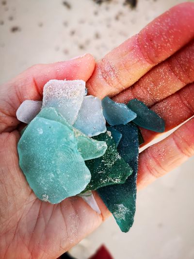 Close-up of hand holding sea washed glass, sandy palm with holding colourful glass on the beach