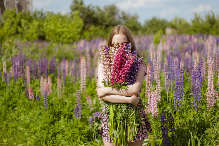 Young woman in the field of flowers with bunch of lupines