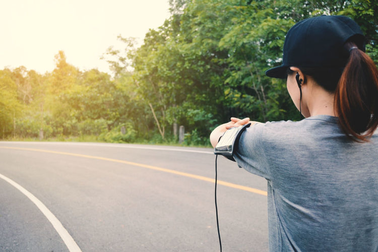 Rear view of woman listening to music while stretching on road